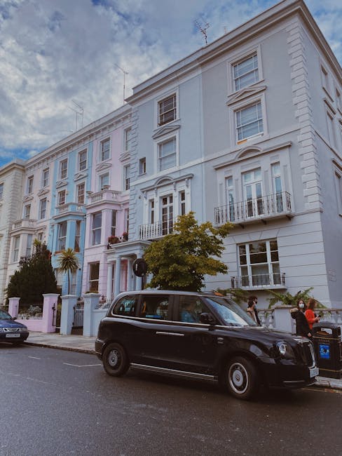 Exterior view of a pink, rounded, multi-storey building with four visible windows on each floor, situated at a street corner. The building's curved façade features white window frames and a decorativ